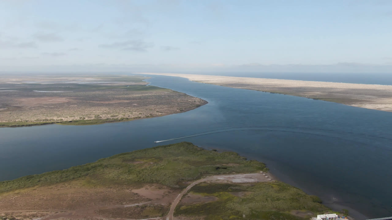 Aerial view in Aldofo Lopez Mateos, Baja California Sur, showing a broad blue channel between low brown-green land and pale sand flats, with the boat wake shifted slightly farther across the lower water and no visible people.