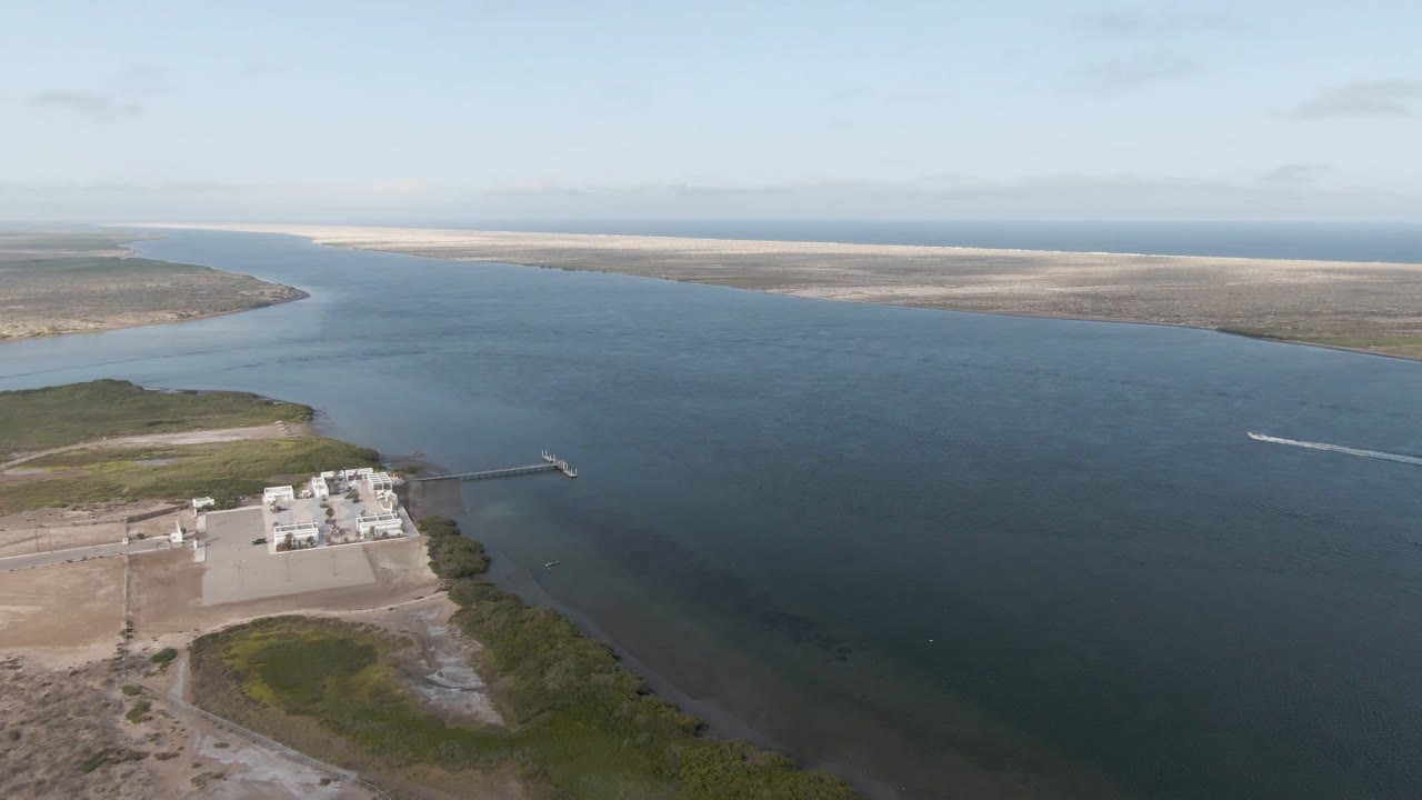 At 0:02, the Baja California Sur shoreline remains in the lower left while the broad water channel fills the frame, with sandbars on the far side, a small wake near the right edge, and no visible people.