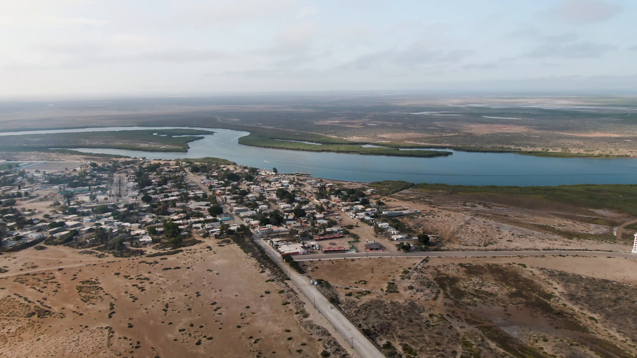 Aerial view of a small settlement beside a wide river and dry scrubland.