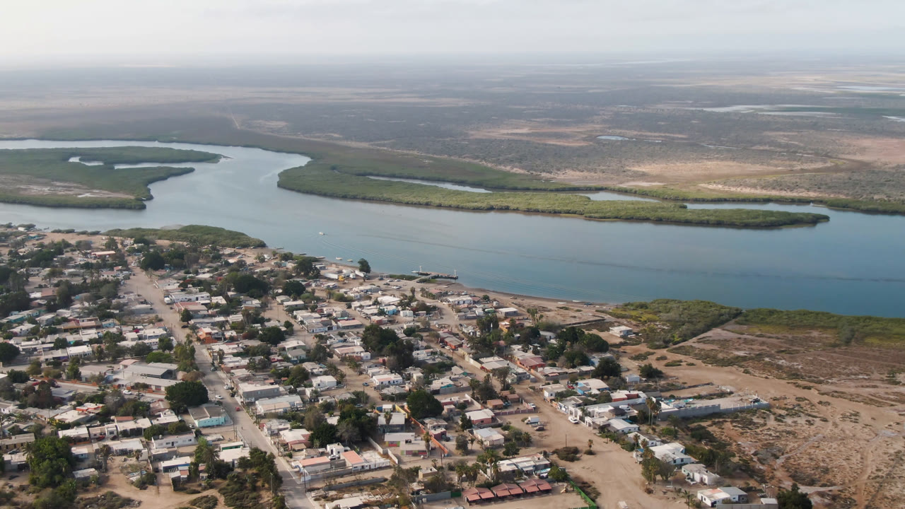 Village rooftops below a river bend and green mangrove island