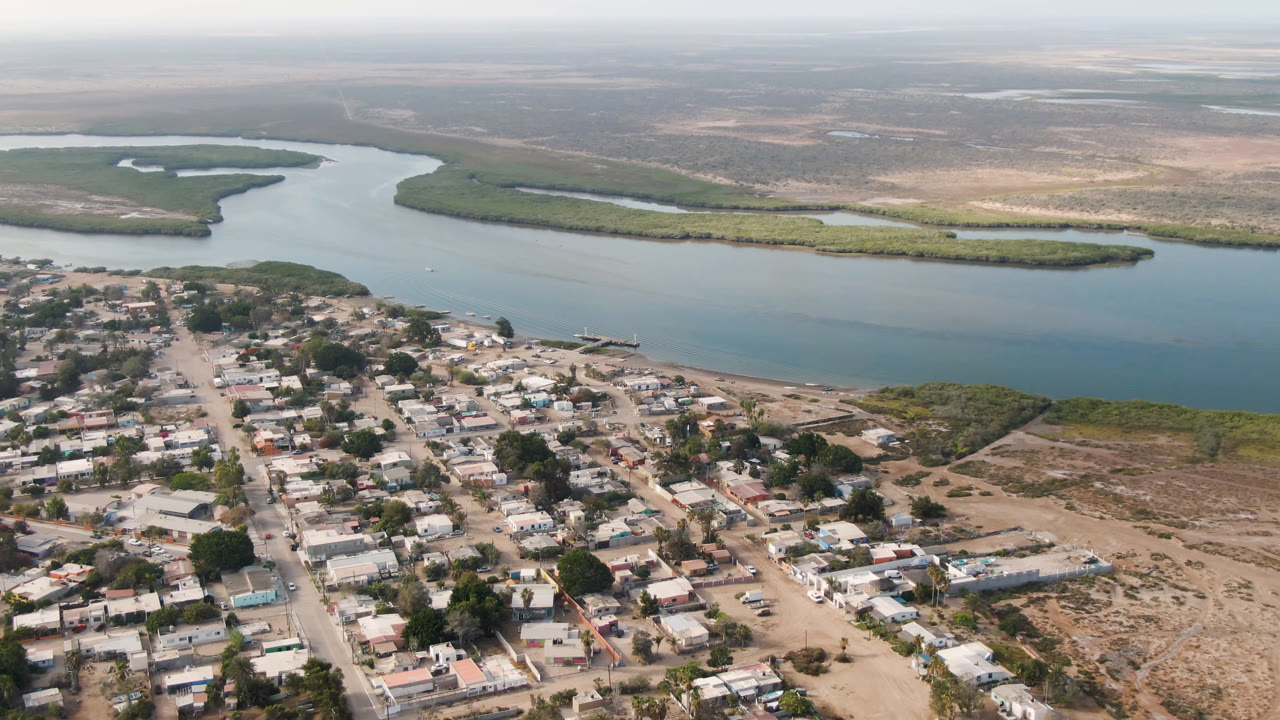 Elevated view of low buildings, dirt roads, river, and mangroves.