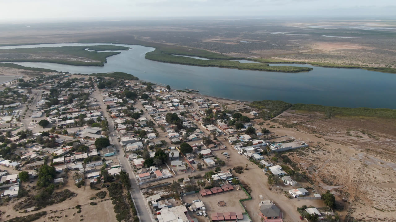 Aerial view of a small town beside broad blue water and dry coastal land.