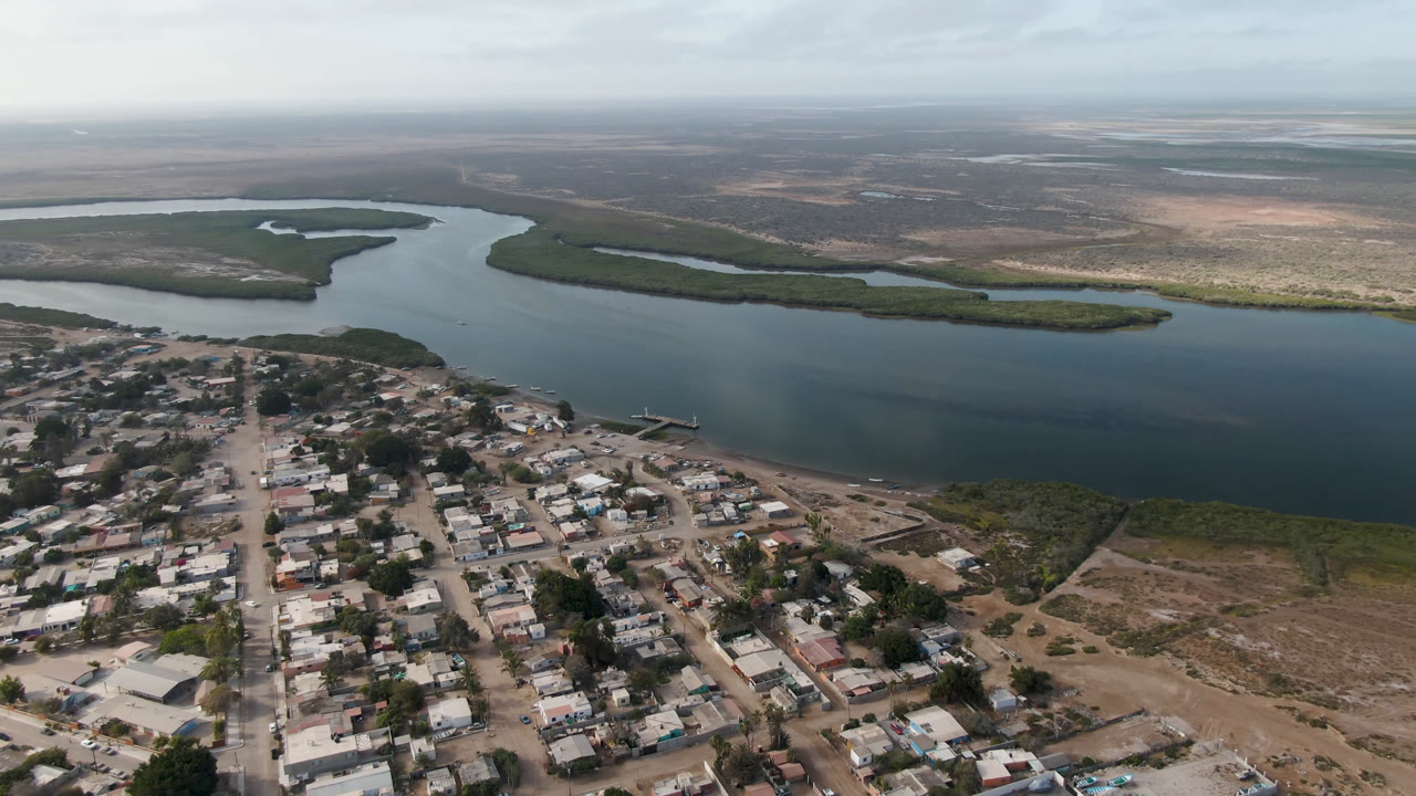 Aerial view of a small town beside a wide river channel and green shoreline vegetation.