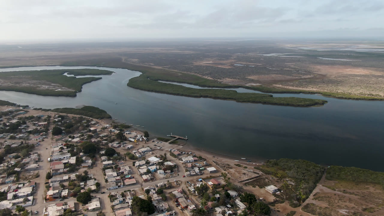 Aerial view of a small town beside a broad river delta under cloudy sky.
