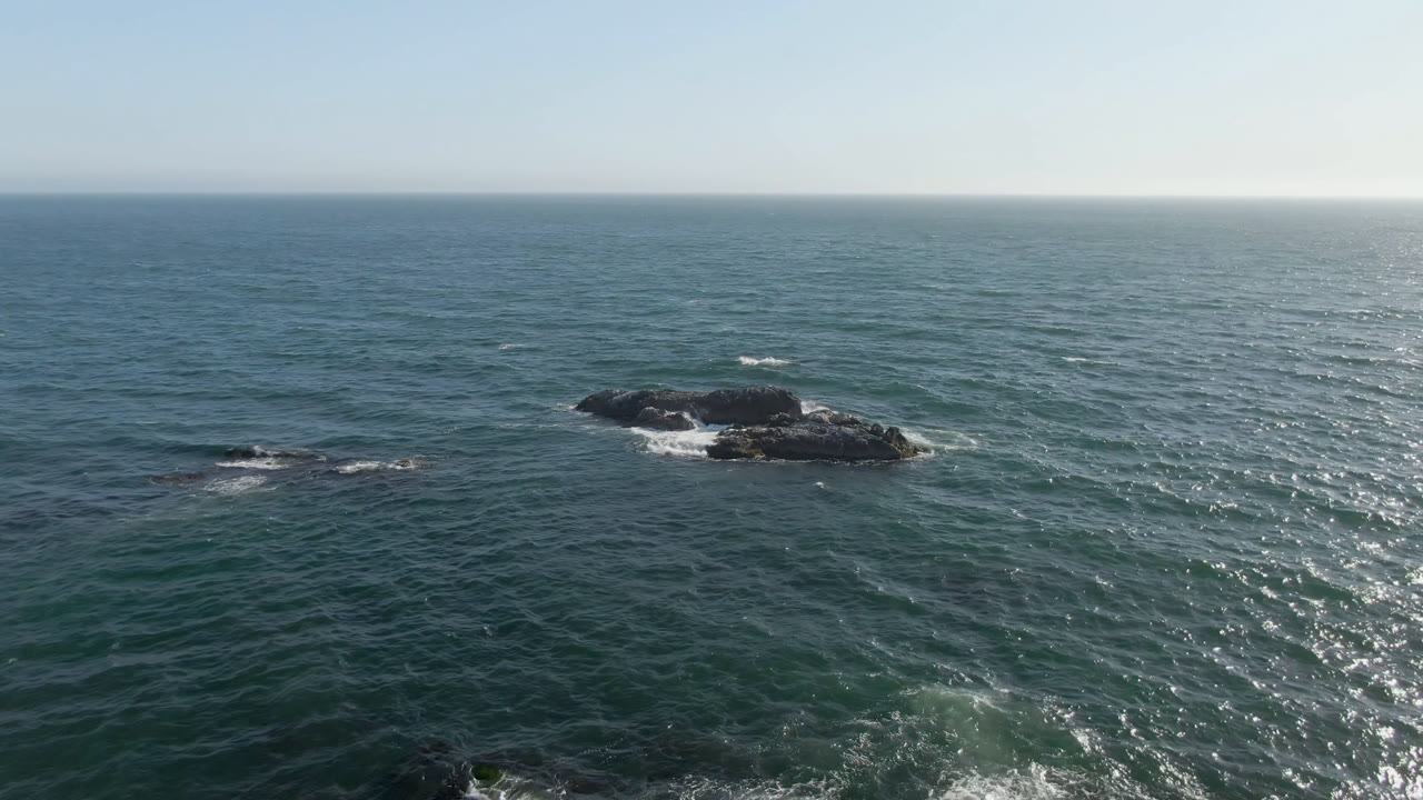 Rocky islet surrounded by ocean under a clear horizon.