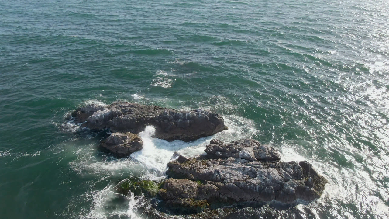 Overhead coastal rocks with waves breaking between them.