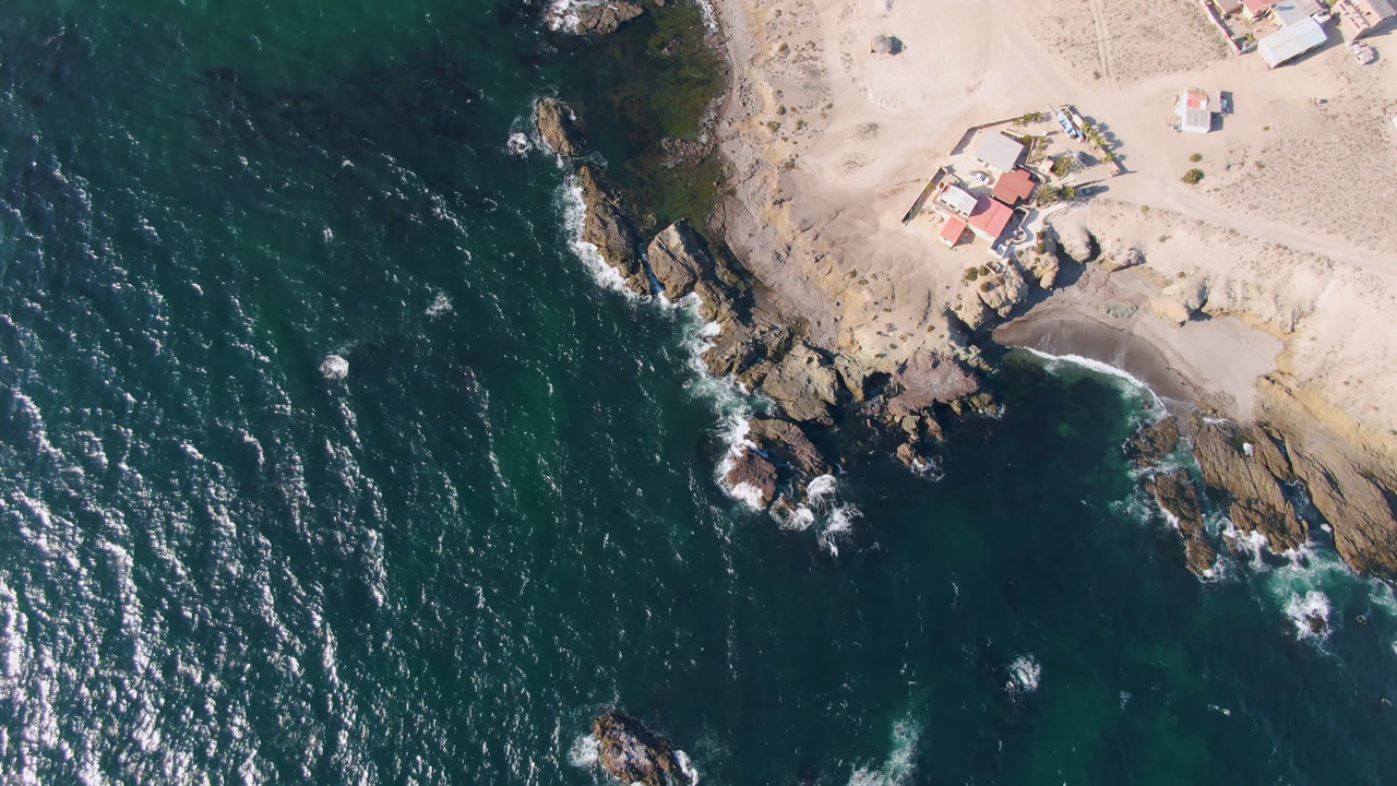 Top-down coastal water with rocks, sand, and shoreline buildings
