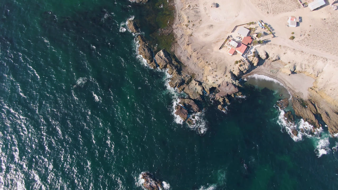 Overhead coastal view with ocean, rocks, sand, and houses