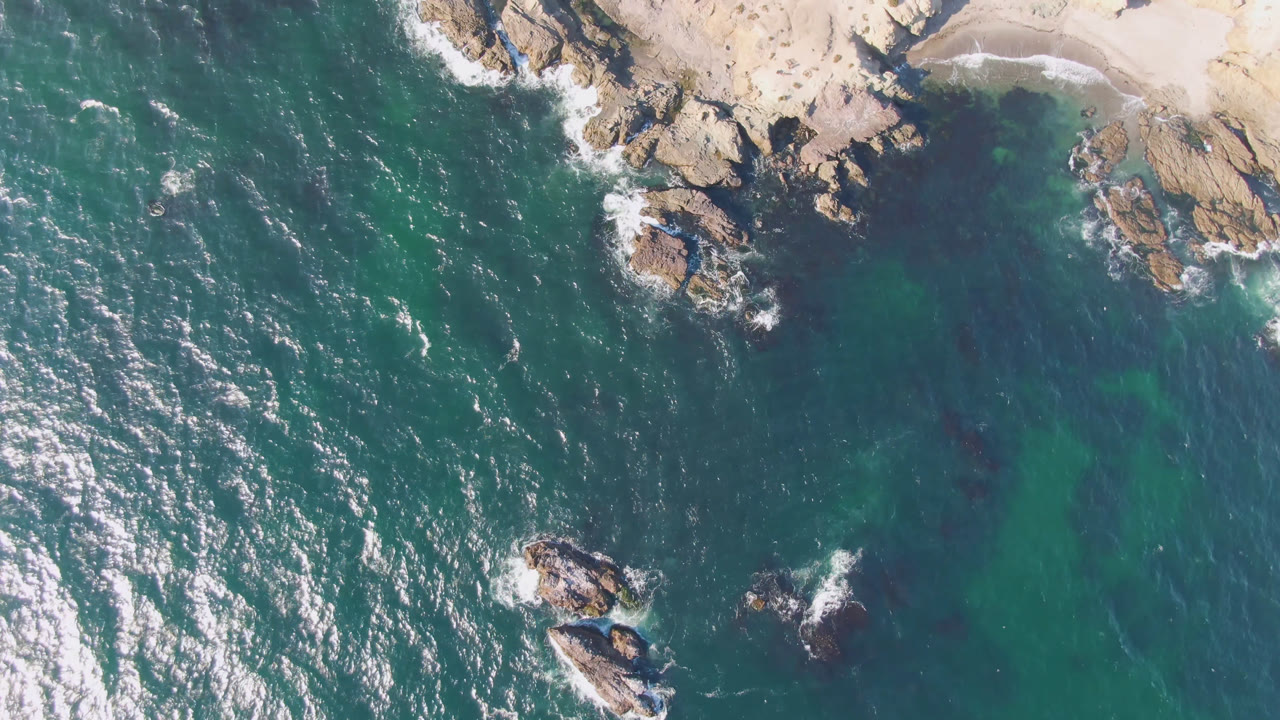 Drone view of waves around rocks near a sandy beach
