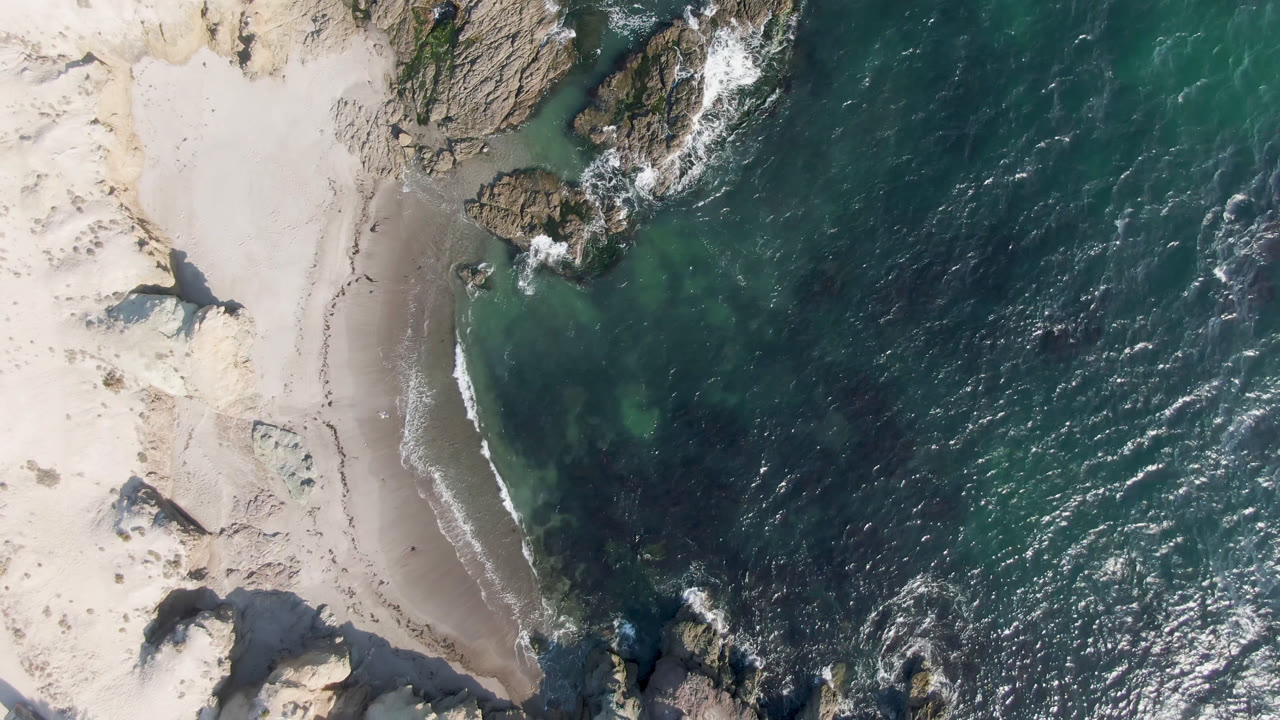 Top-down coastline with sand, rocks, and choppy ocean