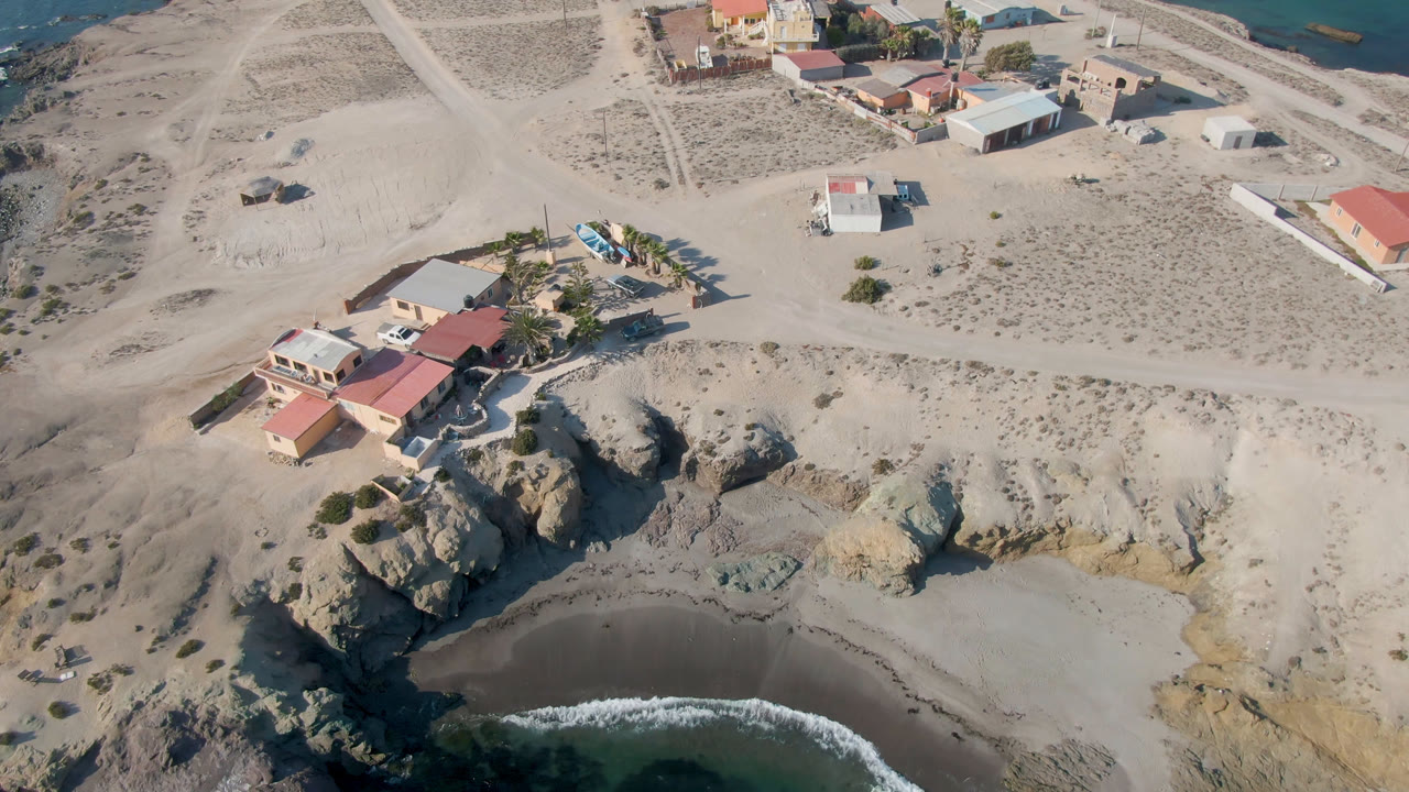 Aerial view of a cliffside house above a curved beach and dark water.