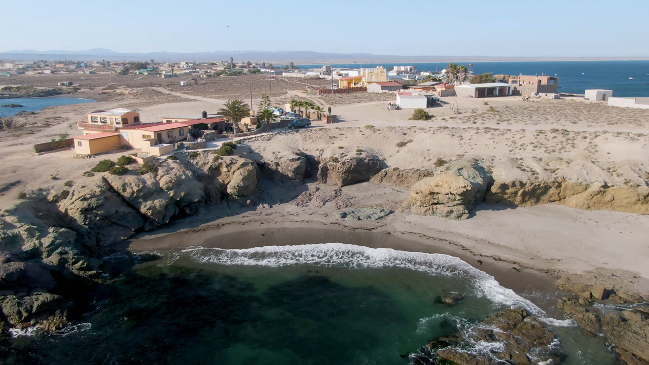 Aerial view of rocky beach, green water, and coastal buildings