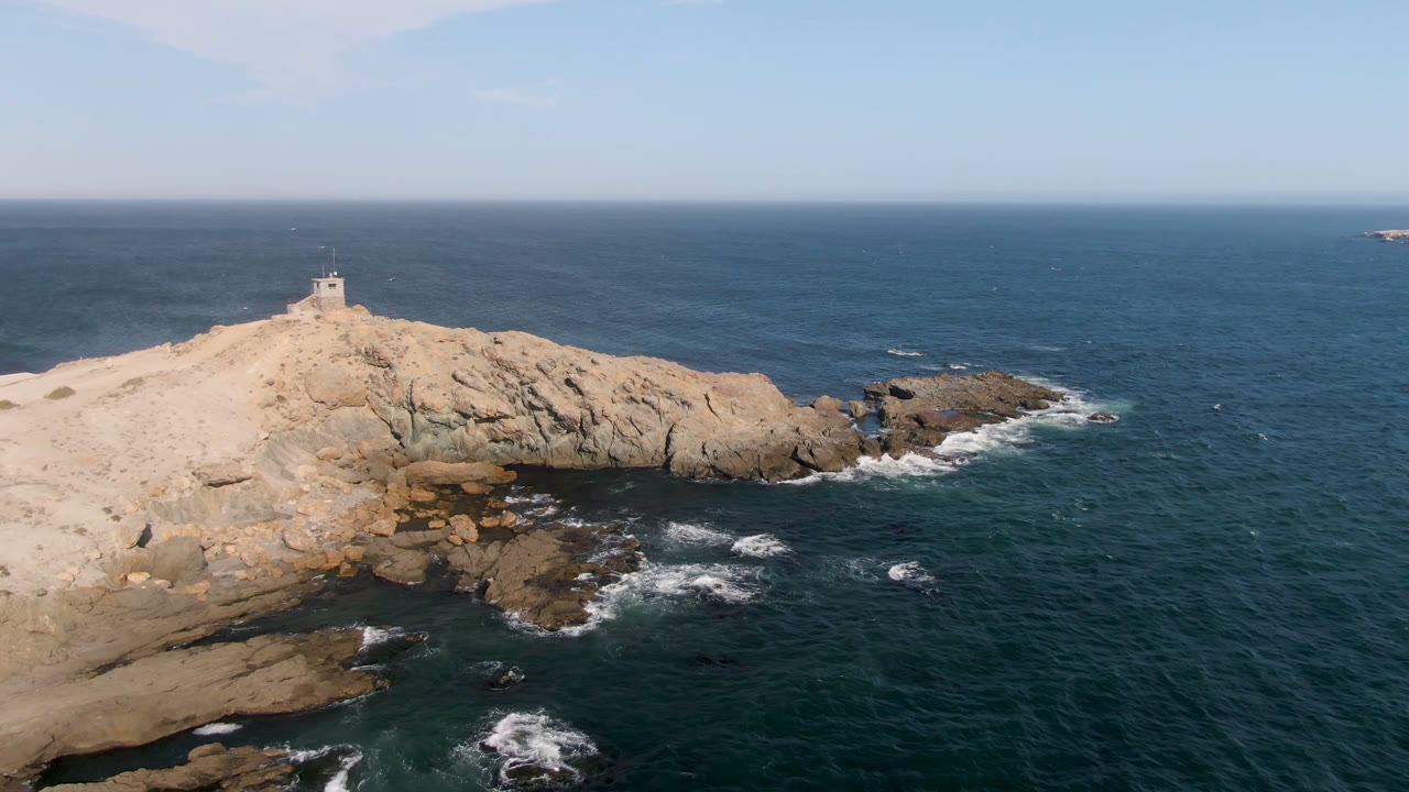 Lighthouse on rocky coast with broad ocean horizon behind it.