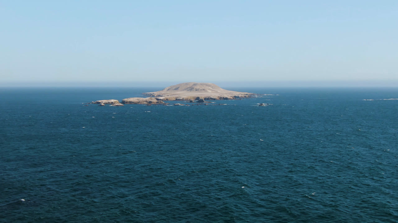 Wide aerial view over blue ocean toward a low rocky island off Bahia Ascuncion, Baja California Sur, with a clear sky and no visible people.