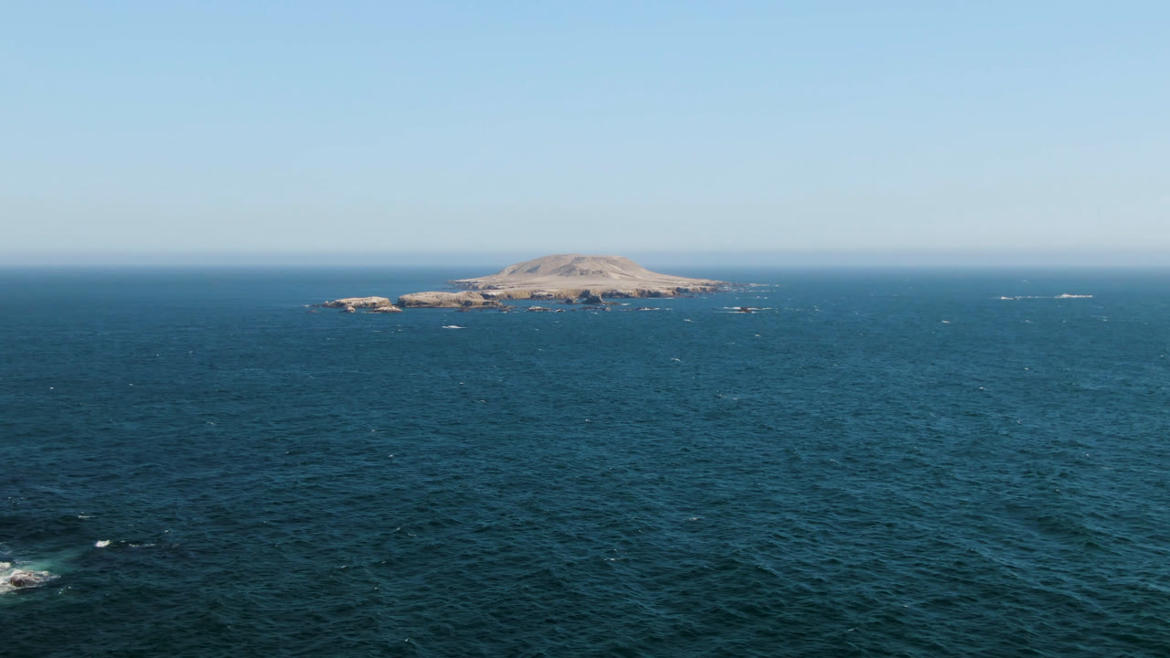 Distant island and open ocean under pale blue sky