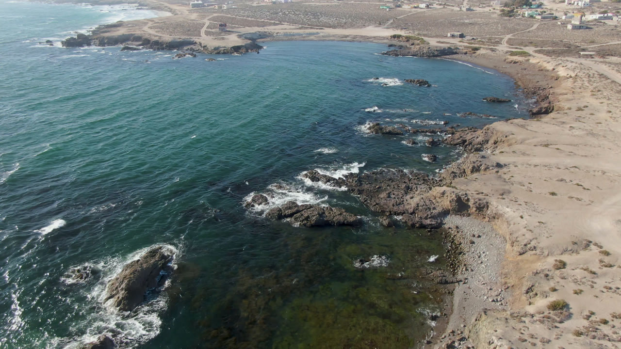 Aerial view of teal ocean, rocky outcrops, and sandy coast