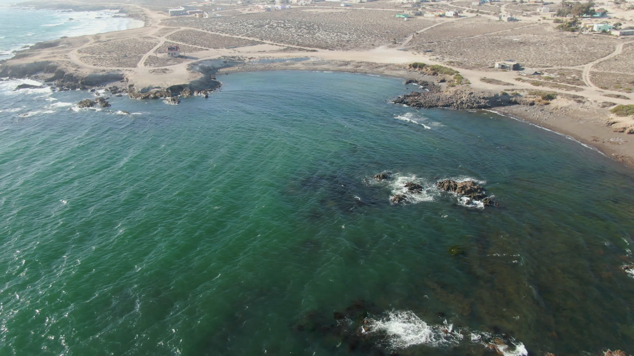 Drone view across a curved beach with rocky points and shallow water