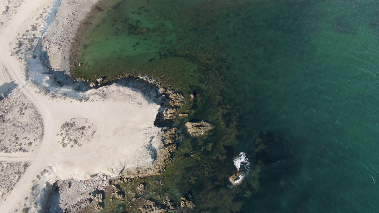 Aerial coastline with pale sand, rock outcrops, and darker water patches.