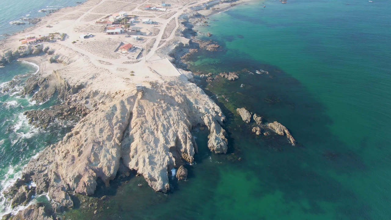 Aerial view of pale rocks, sandy beach, and green-blue ocean water.