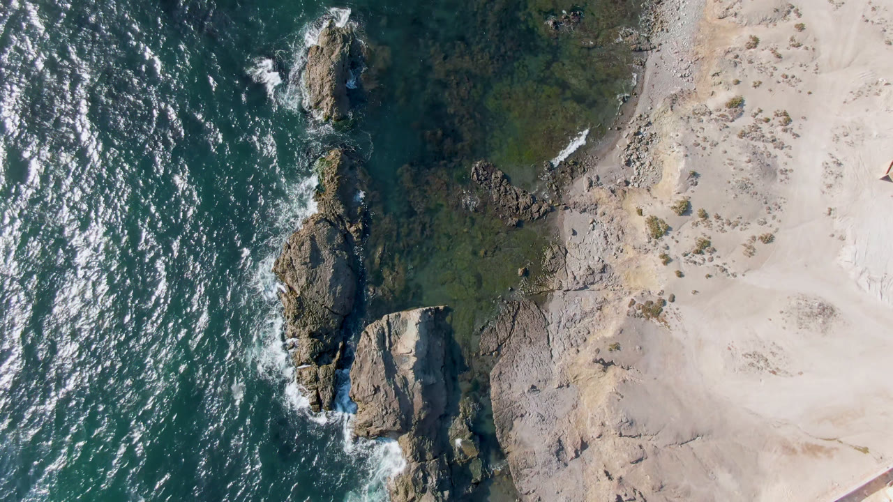 Drone view of rocky shoreline beside bright sand