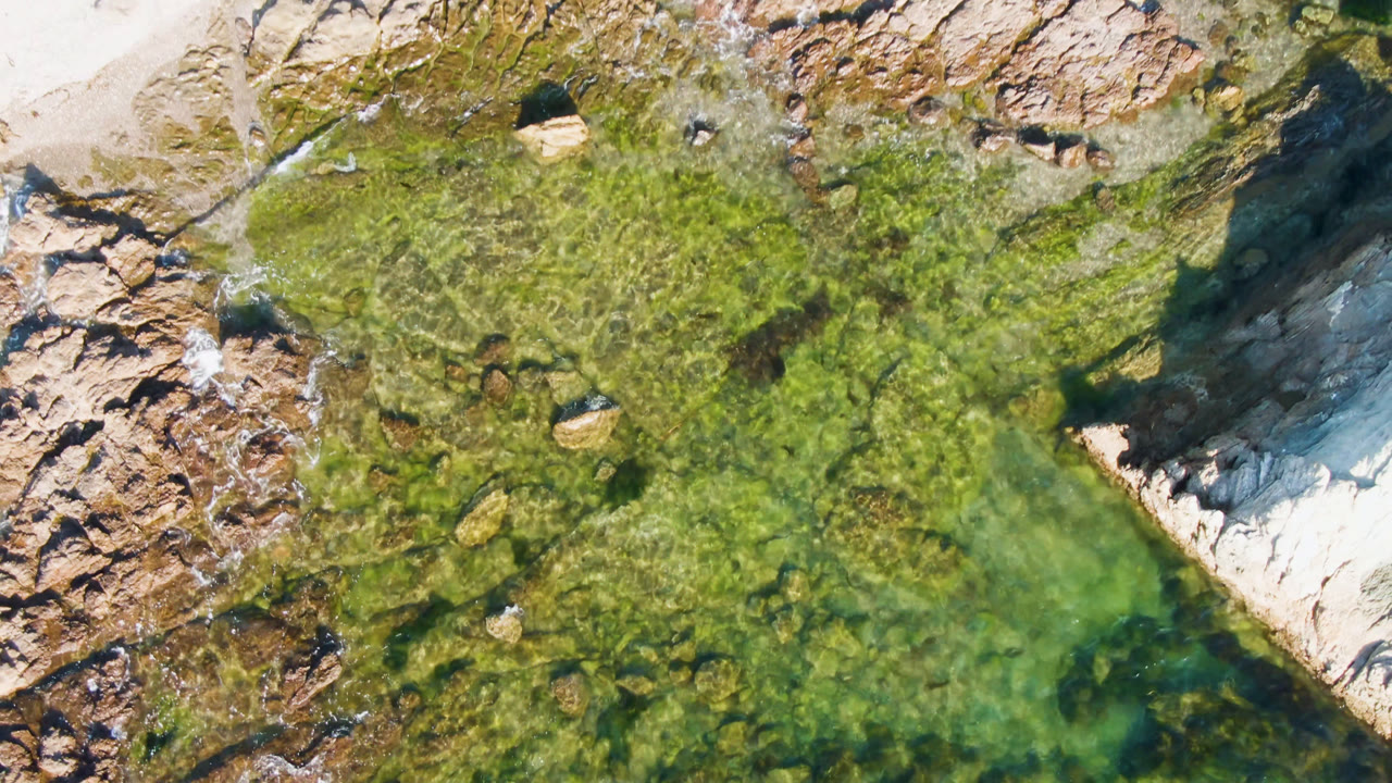 Clear green coastal water beside pale sand and rugged rocks