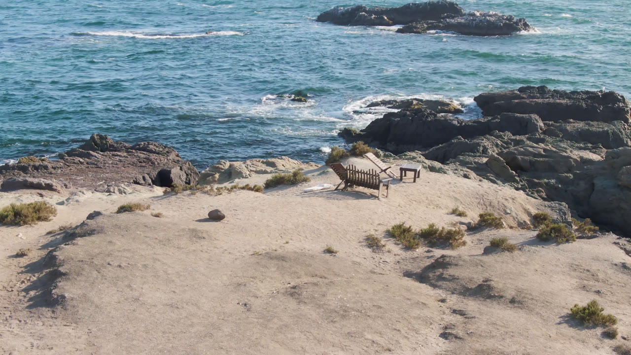 Empty sandy beach with chairs, table, rocks, and blue ocean