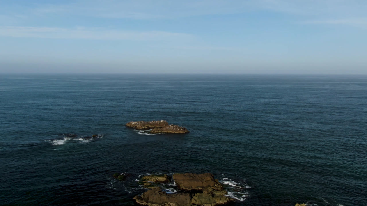 Offshore rocks in blue ocean with low rocky shoreline below