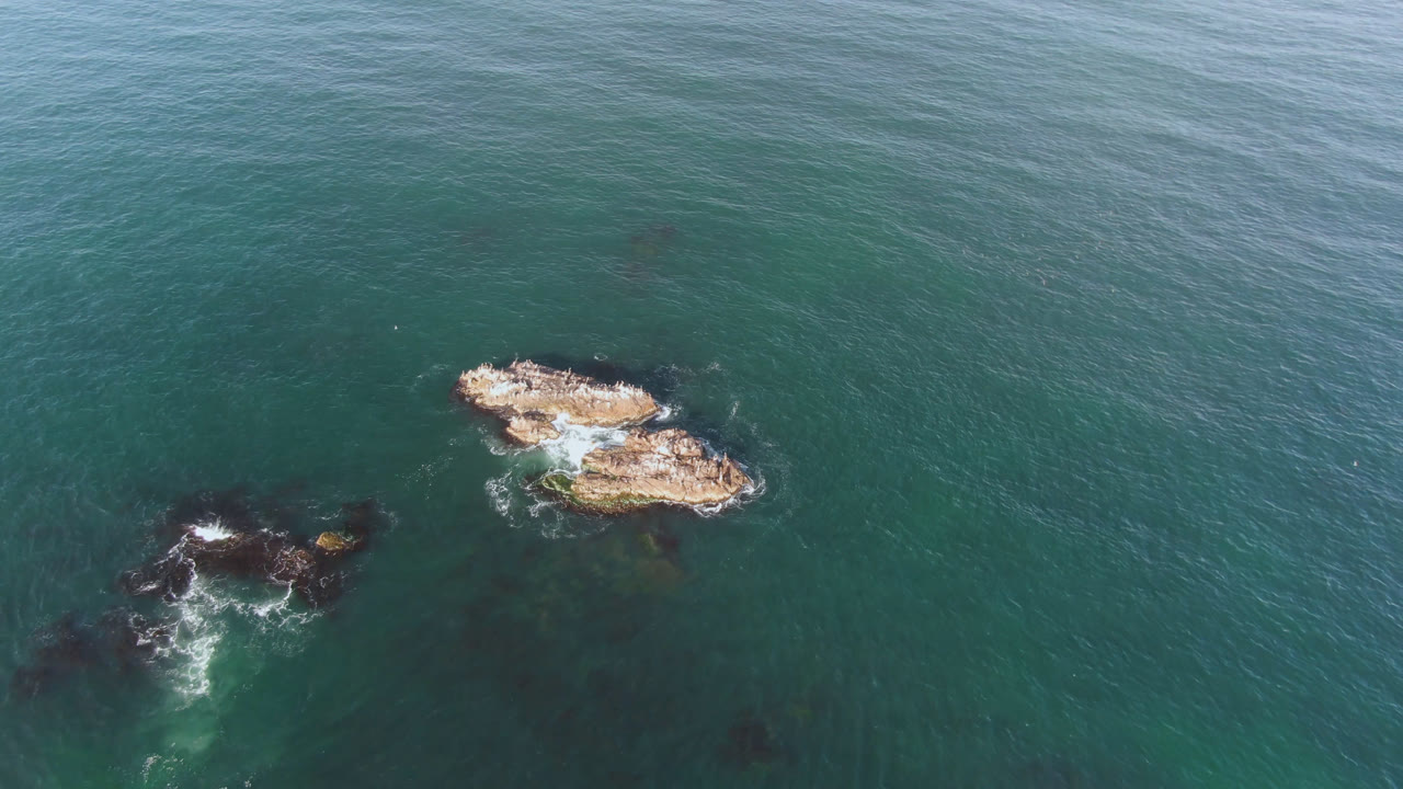 A later overhead view in Bahia Ascuncion shows the two main rocks slightly more centered, with darker underwater patches below them and no visible people.