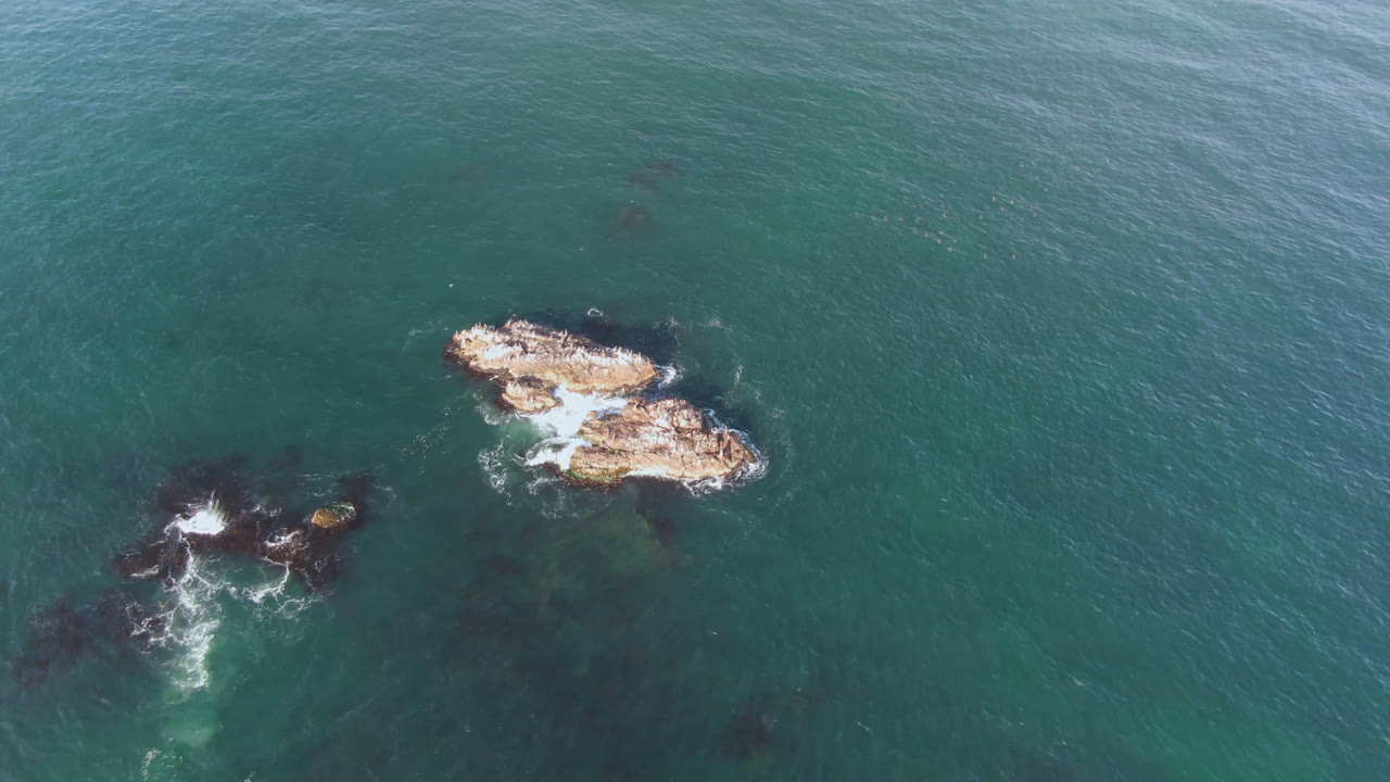Rock outcrops near the upper right with surf on dark rocks below