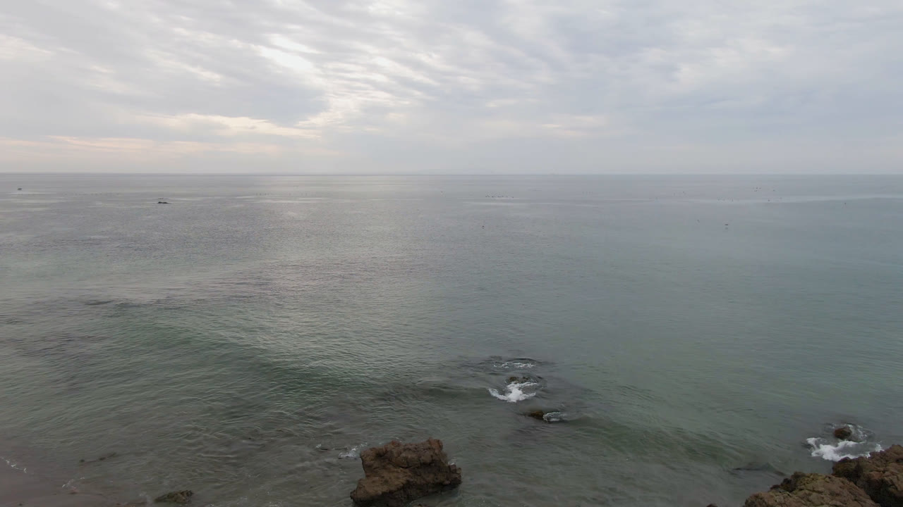 Cloudy ocean horizon with rocks and small surf in the foreground.