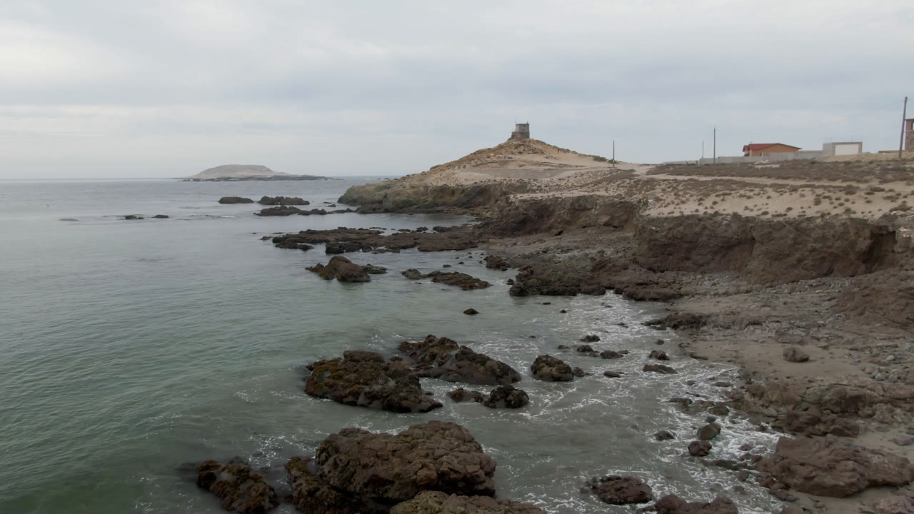 Rocky ocean shoreline with a distant lighthouse under cloudy sky