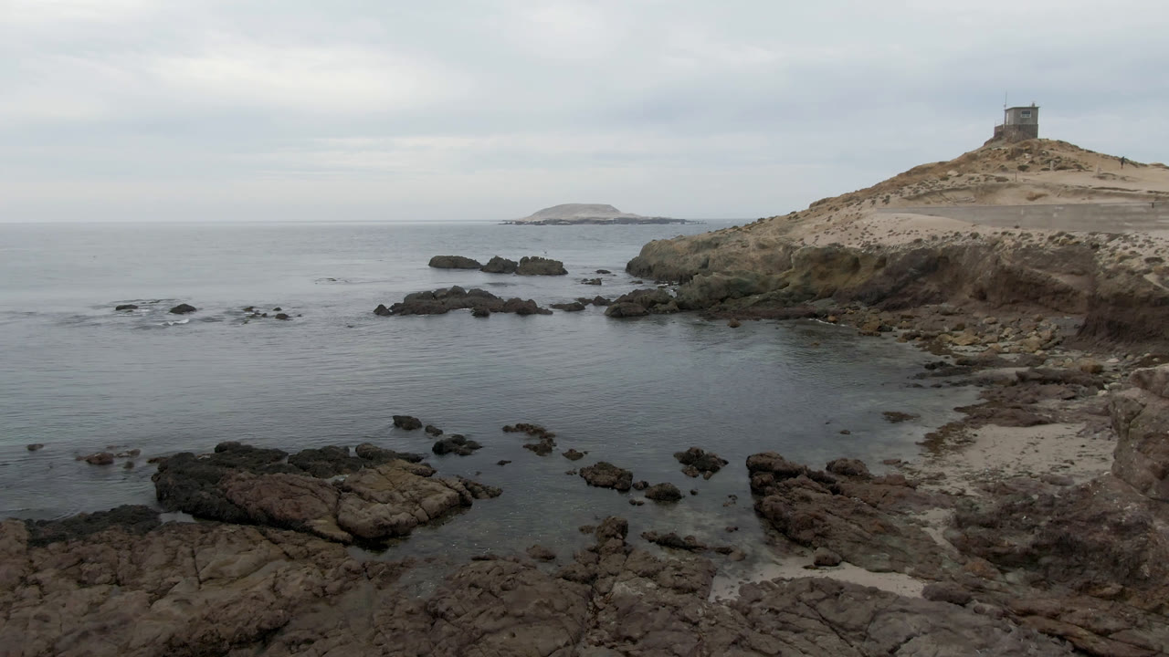 Rock shelves in shallow water with lighthouse hill and distant island.
