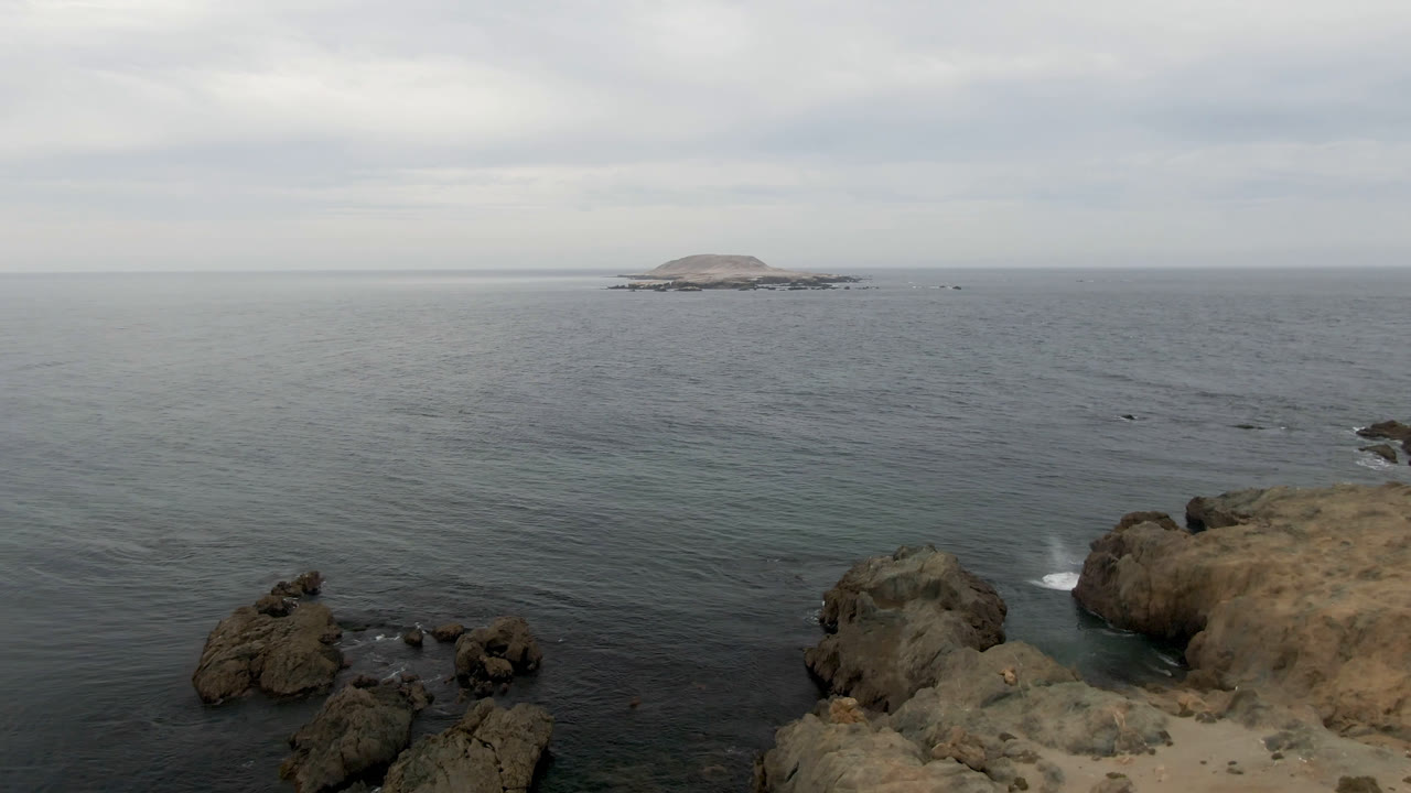 Wide ocean view with rocky shore and distant island under clouds