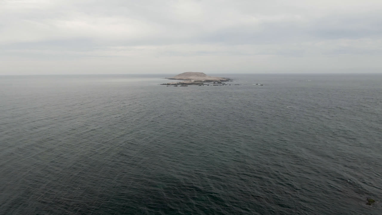 Opening frame of Bahia Ascuncion, Baja California Sur, showing textured dark ocean in the foreground, a small low island near the horizon, gray cloud cover, and no visible people.