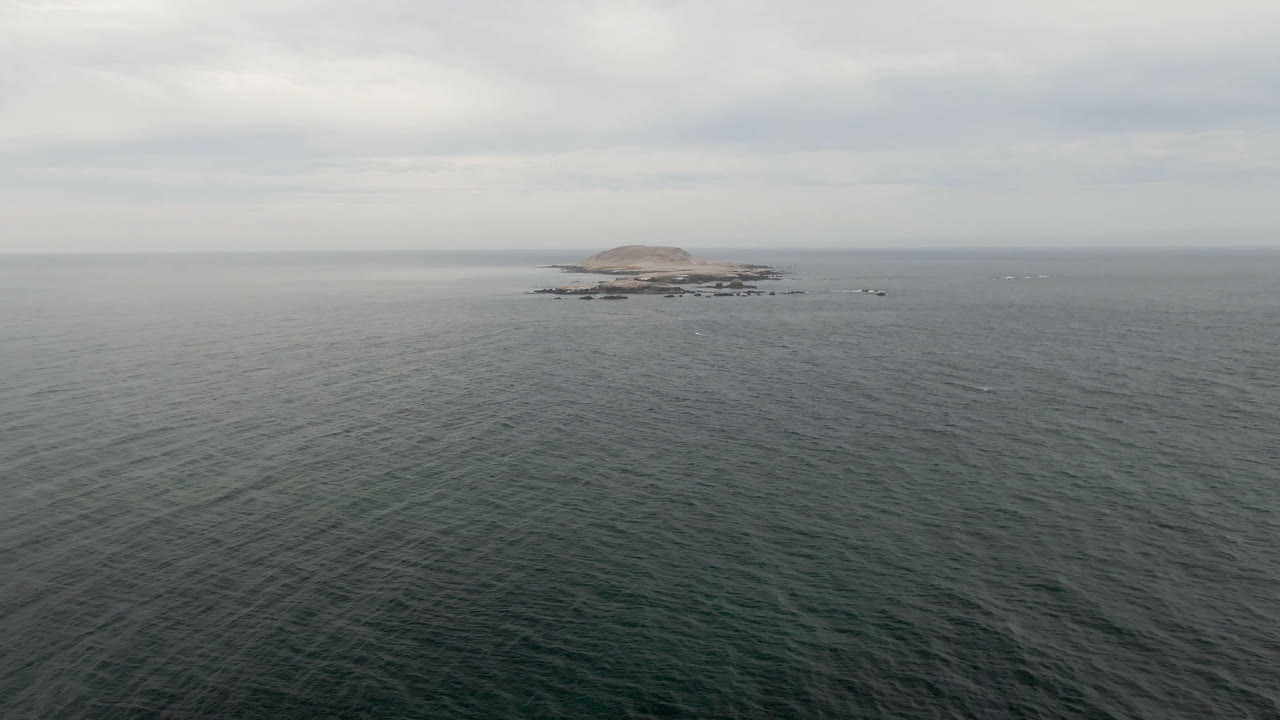 Small island and rocks on the horizon beyond a broad expanse of ocean.