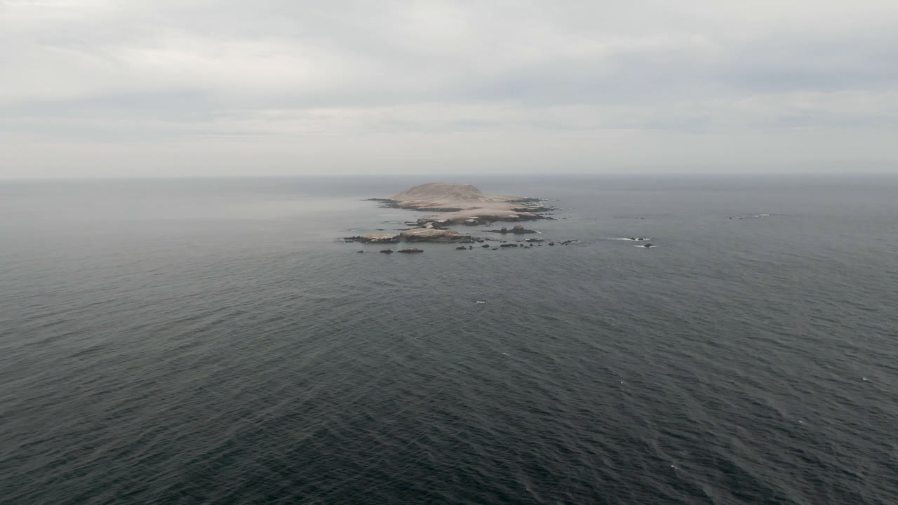 At 0:01, the Bahia Ascuncion aerial keeps the rocky island centered above textured ocean water, with a soft gray sky and no visible people.