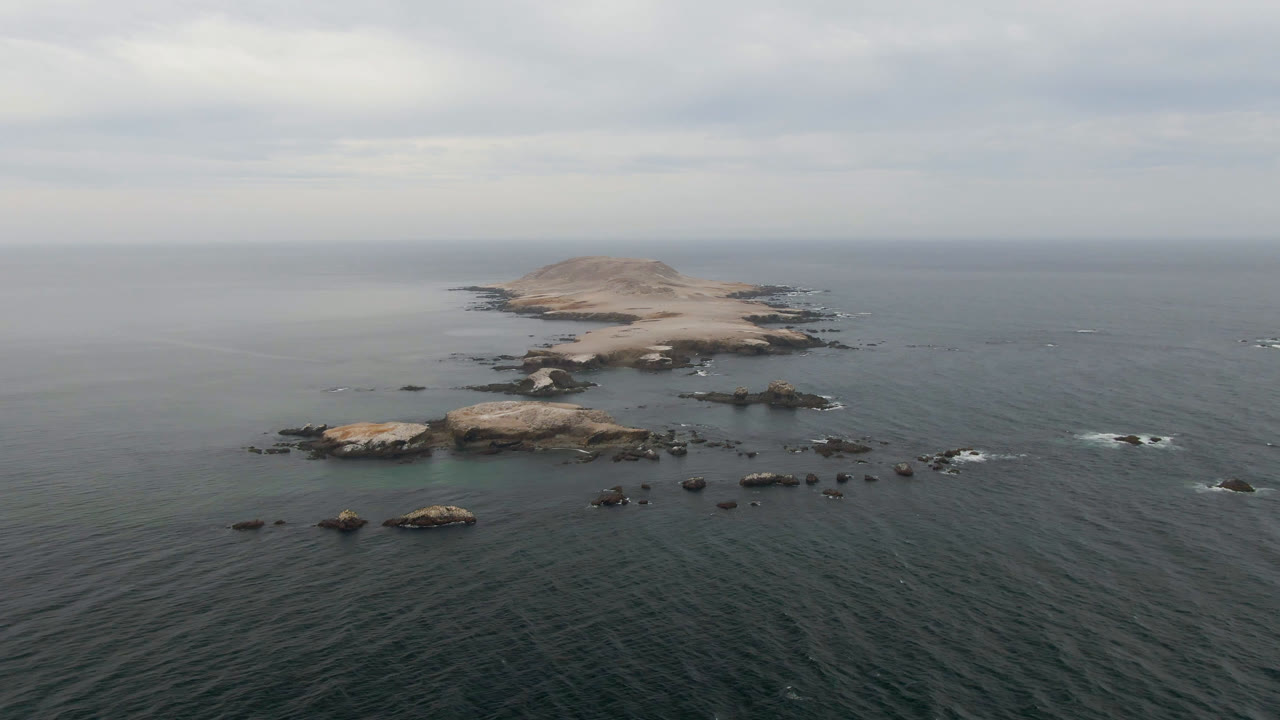 Rocky offshore island surrounded by calm ocean and white wave breaks