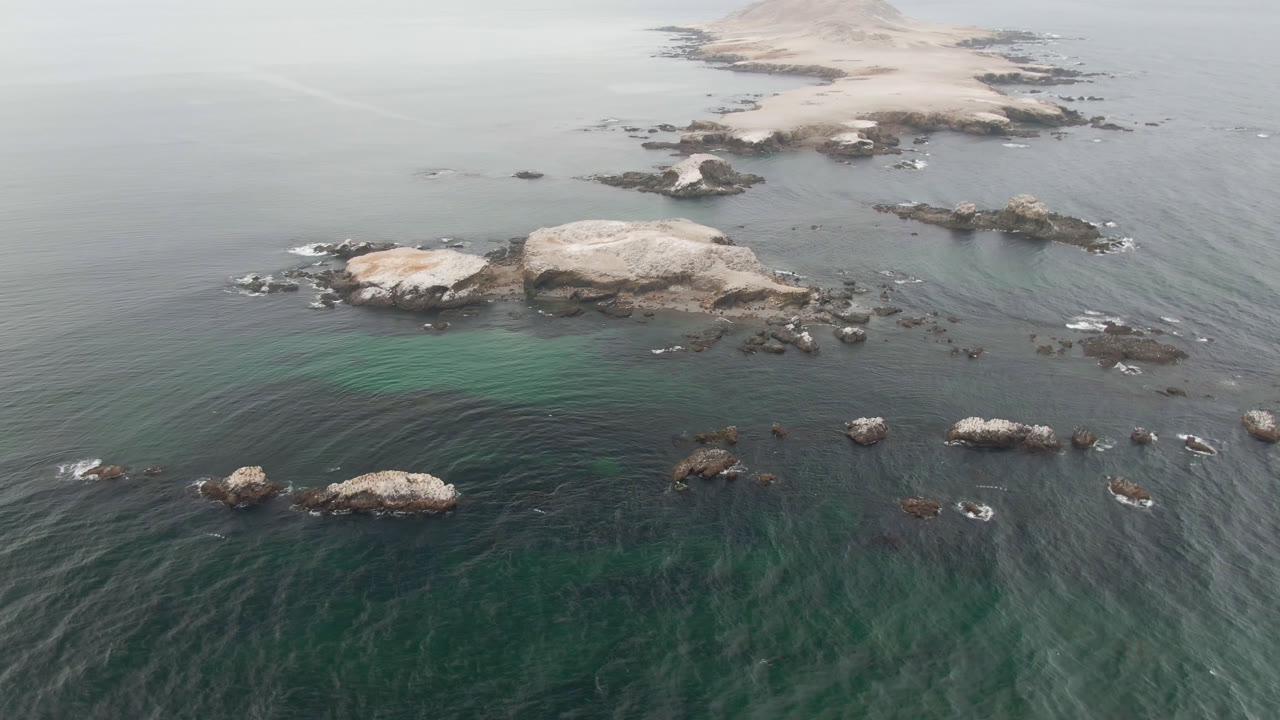 Aerial view of rocky ocean coastline and a low island beyond.