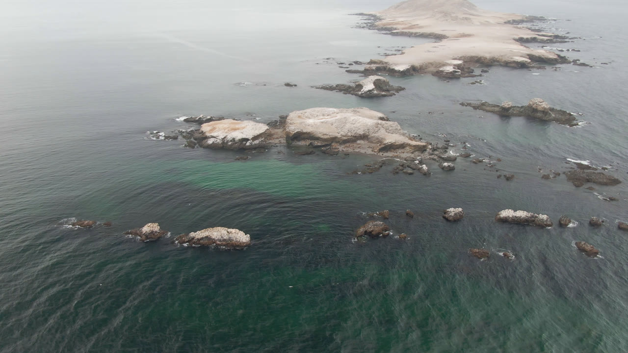 Drone view of scattered rocks across green and gray ocean water.