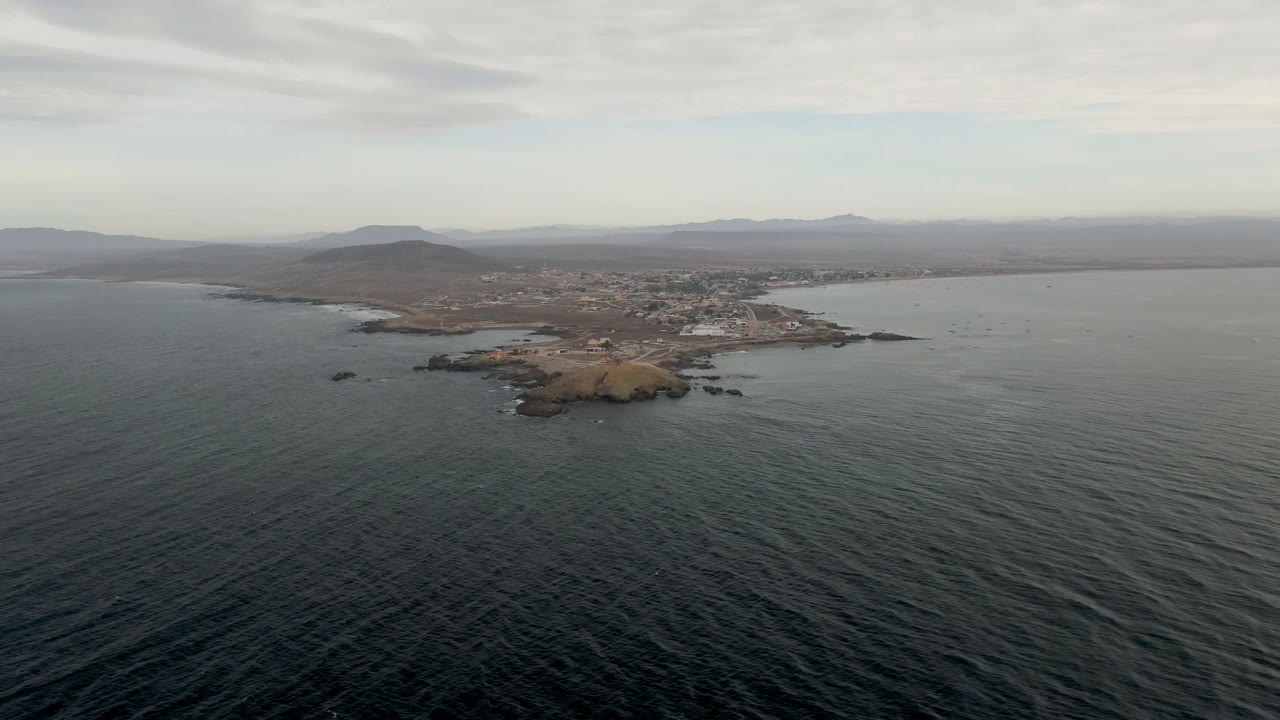 Drone view of small island, open sea, coastal settlement, and low hills