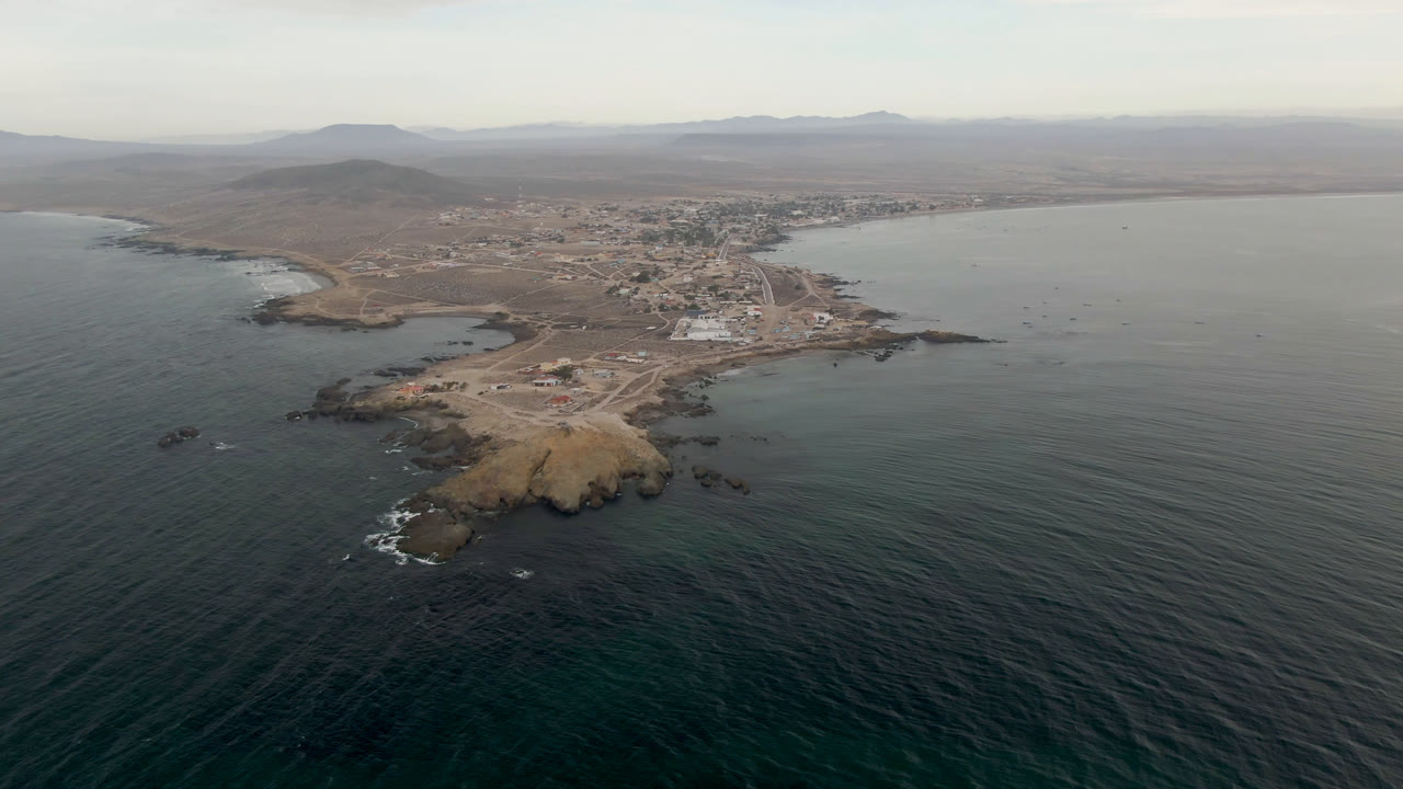 Aerial view of dark ocean water, rocky point, and small coastal town.