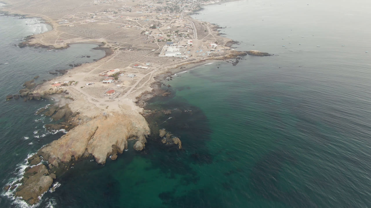 Aerial view of rocky sandy point, turquoise water, and small coastal town.