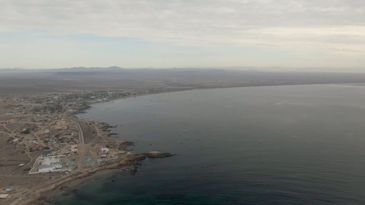 High coastal view with water, sandy land, buildings, and distant hills.