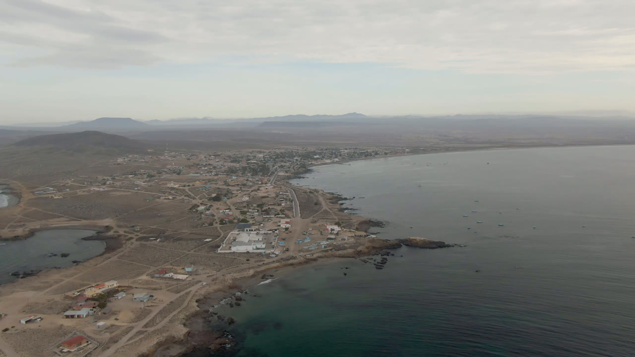 Aerial view of a coastal town beside a broad bay under cloudy sky.