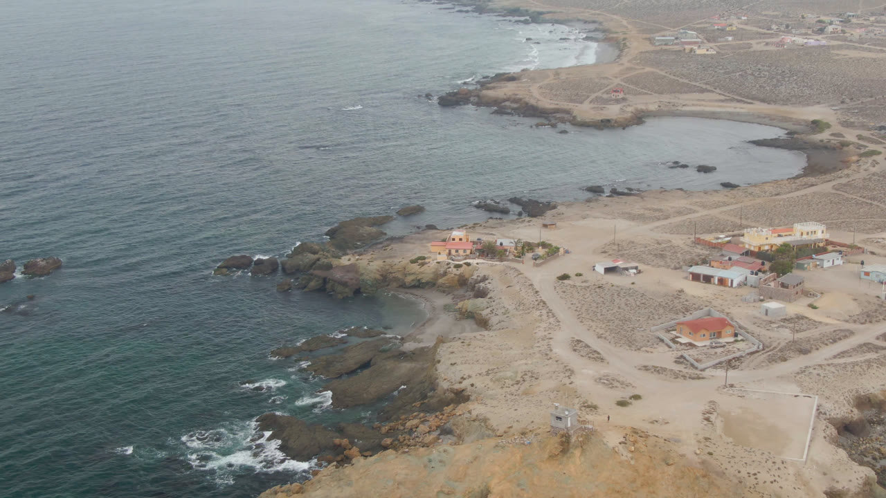 Aerial view of ocean, rocky shore, sandy roads, and small coastal buildings.
