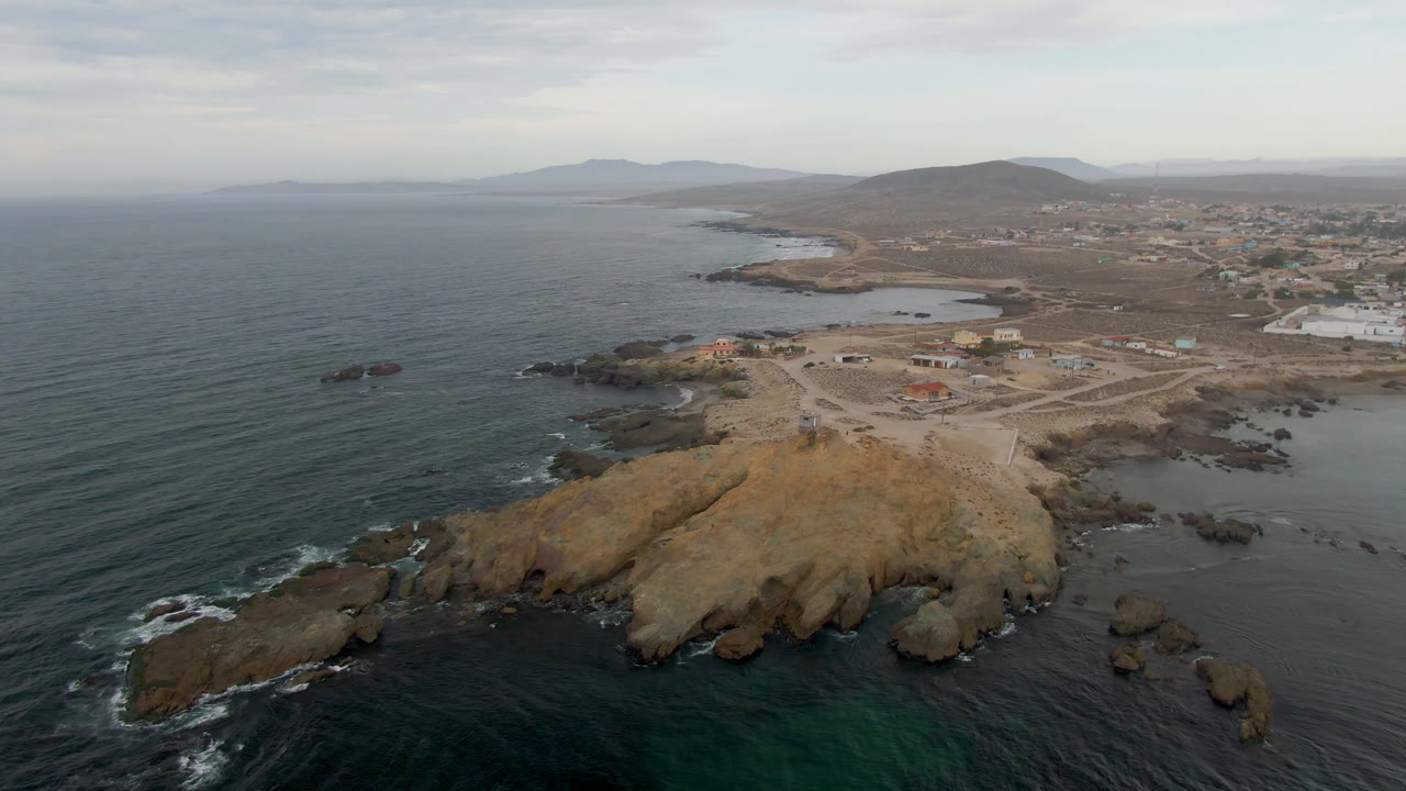 Wide aerial of rocky shore, open water, town, and hazy hills