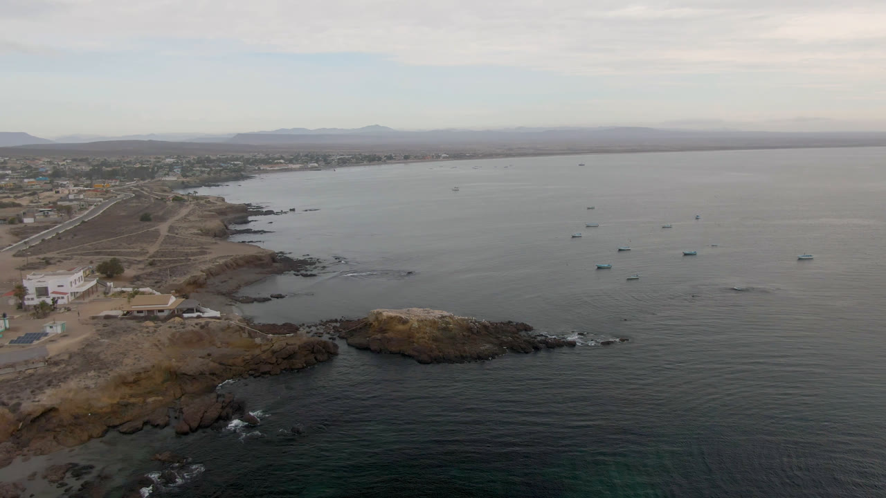 Rocky coastal point below a drone with boats scattered offshore