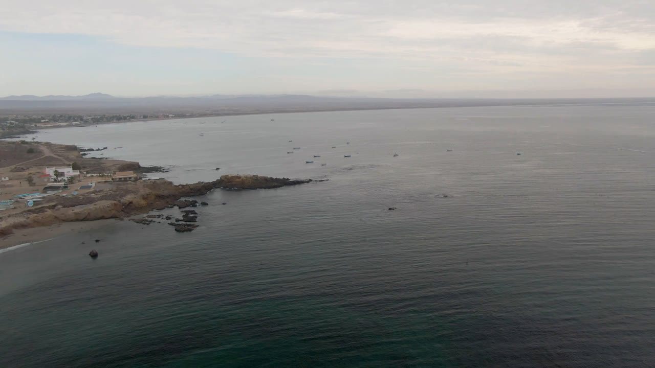 Wide aerial frame of boats on gray ocean beside a rocky shoreline.