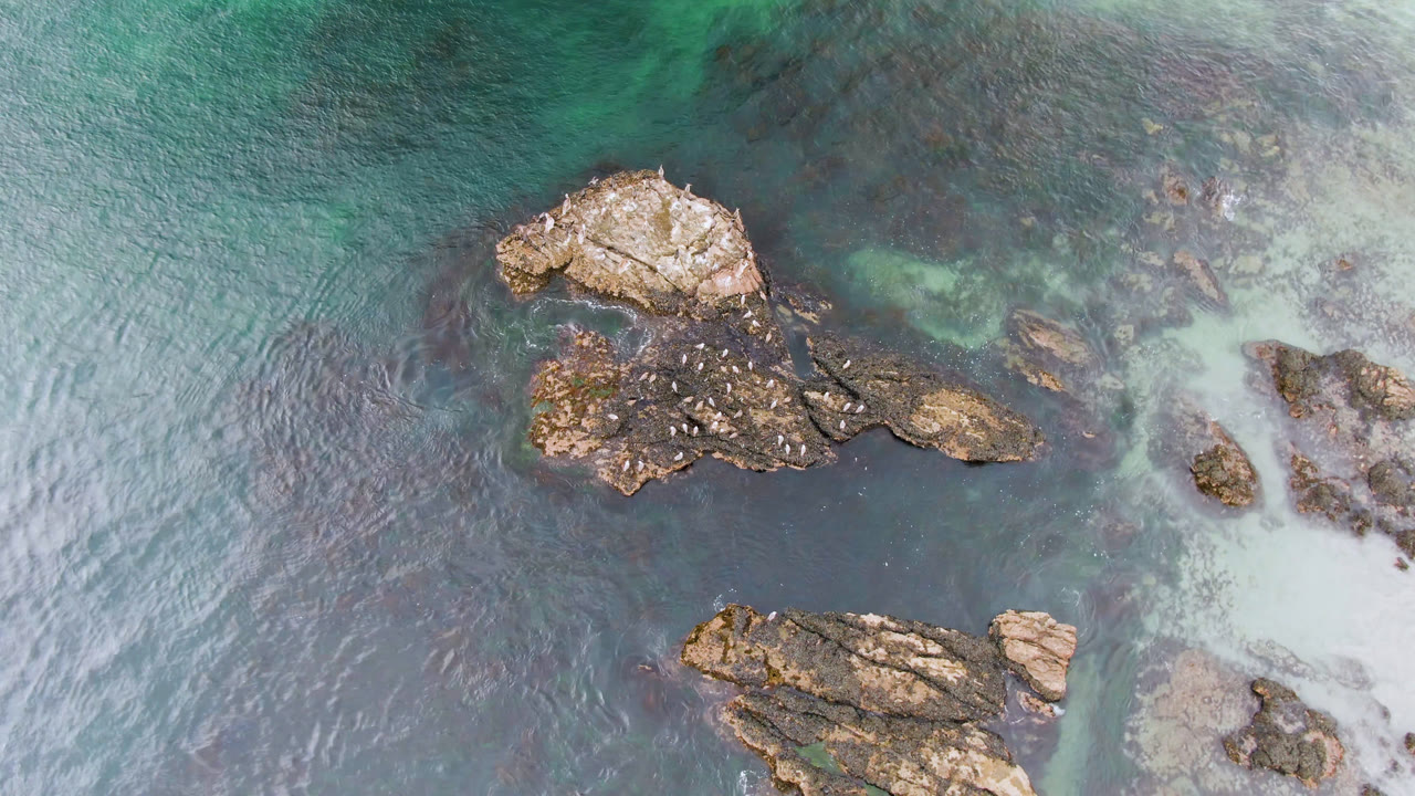 Aerial Bahia Ascuncion view with the main rock cluster near the upper center, a lower rock shelf entering the bottom edge, and no visible people.