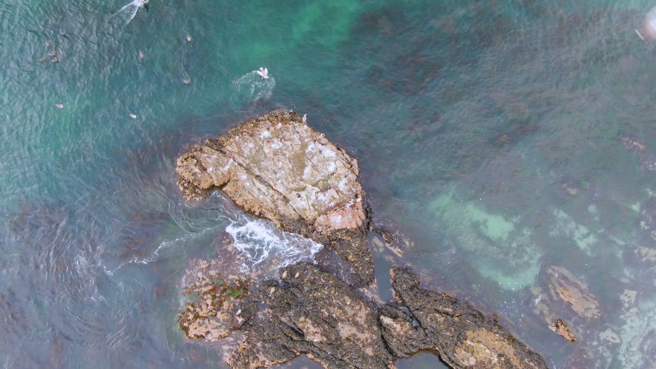 Overhead view of rocks surrounded by blue-green water.